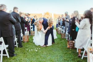 An outdoor wedding ceremony with guests seated on white chairs and dried pampas grass decorations.