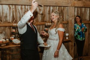 A couple shares cake during their rustic barn wedding reception.