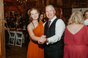Guests dance together at a rustic barn wedding reception with string lights and wooden details.