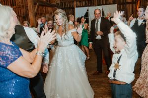 A bride in a sparkly white gown dances among guests at a rustic barn wedding reception.