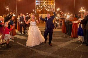 Wedding guests hold sparklers forming an illuminated exit pathway for the newlyweds.