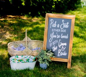 Wedding ceremony sign reading 'Pick a Seat' with decorative baskets on grass.