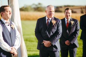 Groomsmen standing at altar during outdoor countryside wedding ceremony.