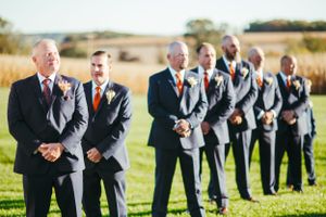 Groomsmen in formal attire stand in line outdoors during wedding ceremony.