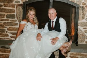 Newlyweds share casual moment while sitting by stone fireplace at reception venue.
