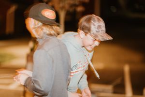Two people wearing baseball caps interact in warm-toned candid moment.