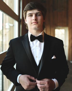 A formal portrait of a groom in classic black tuxedo and bowtie by a window.