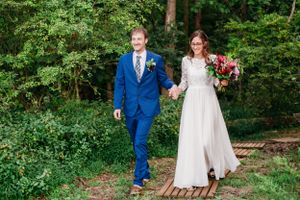 A couple walks along a wooden path through lush greenery at an outdoor wedding ceremony.