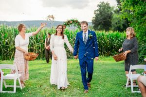 Wedding guests toss confetti as newlyweds walk down aisle at outdoor countryside ceremony.
