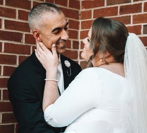 A tender moment between newlyweds against a brick wall background.
