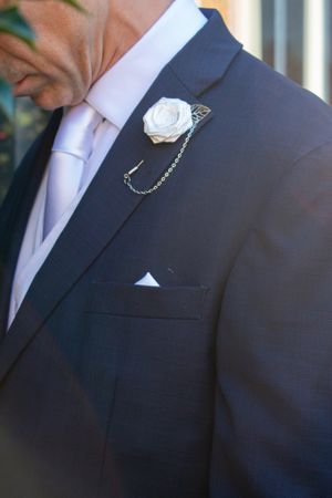 Close-up of a navy suit jacket with white rose boutonniere and chain detail.
