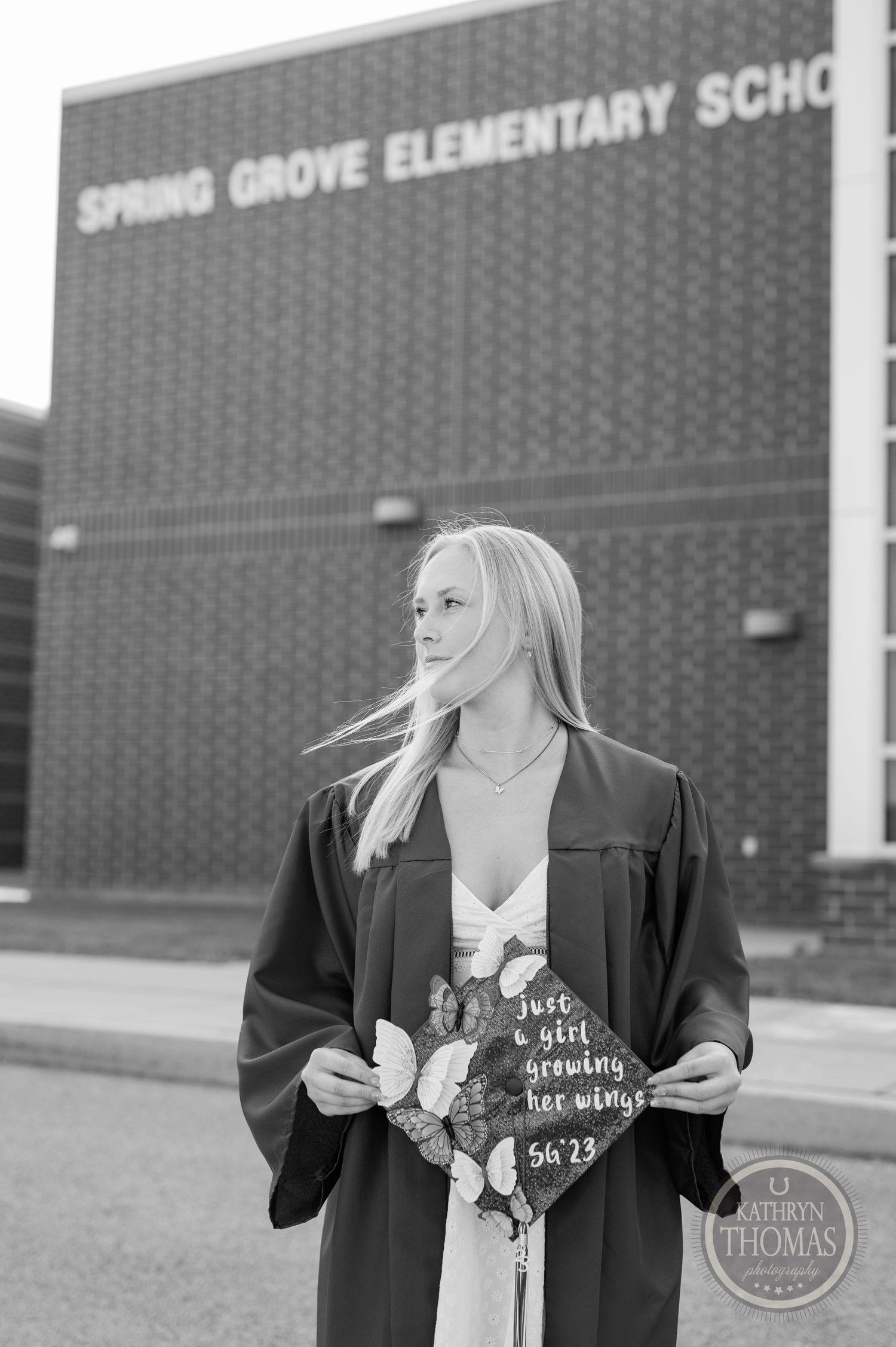 Black and white graduation photo showing decorated cap and flowers outside school building.
