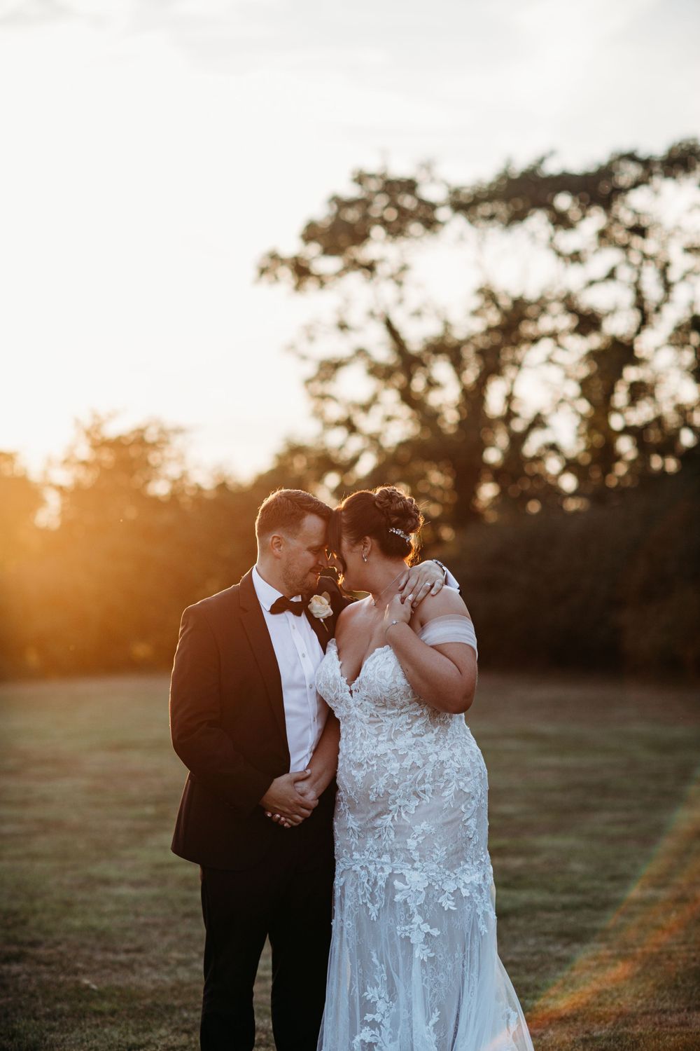 Romantic sunset portrait of couple embracing in formal wedding attire.