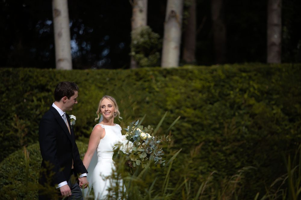 A bride and groom share an intimate moment surrounded by lush greenery and birch trees.