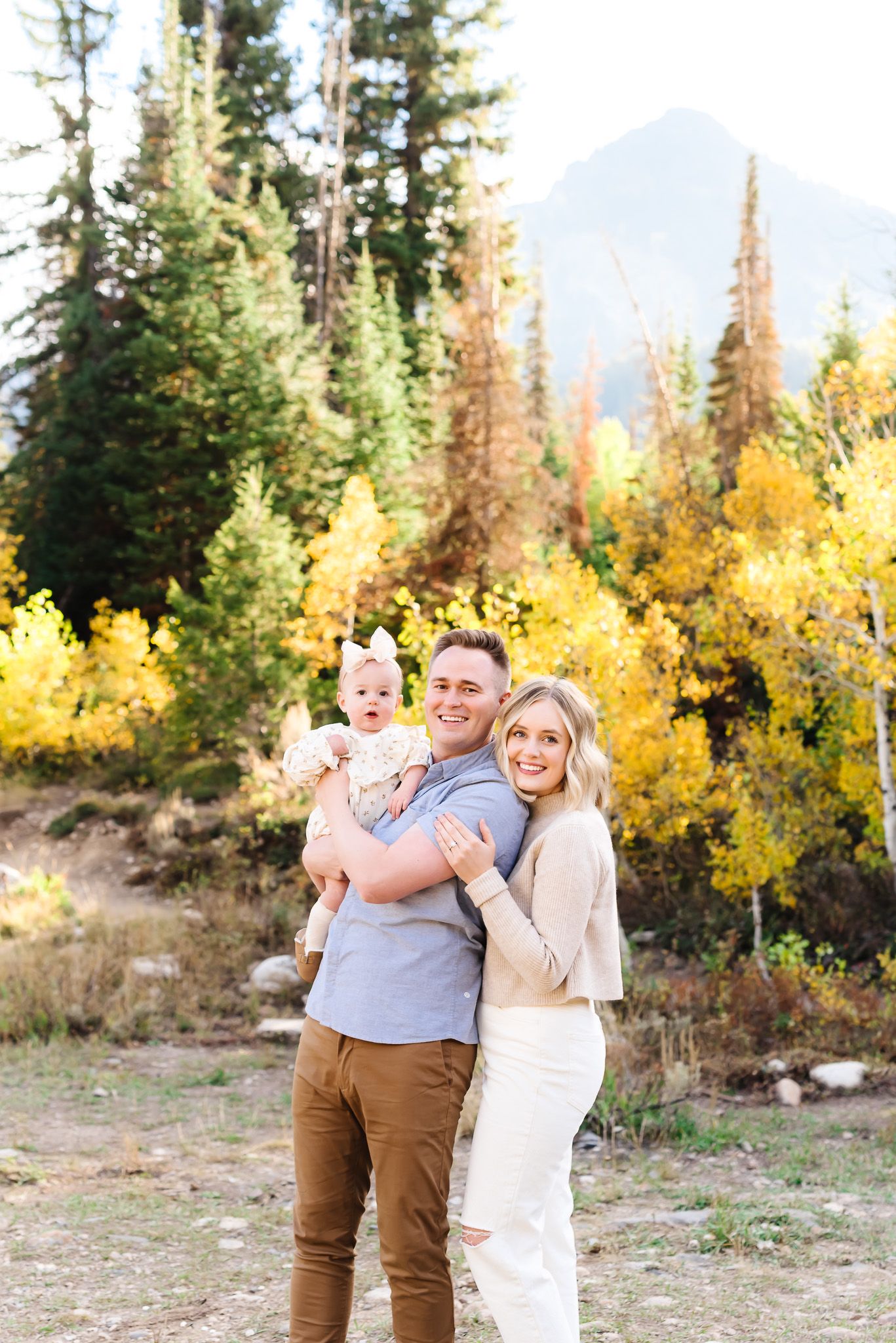 Family embraces and laughs together against backdrop of golden aspen trees in mountain setting.