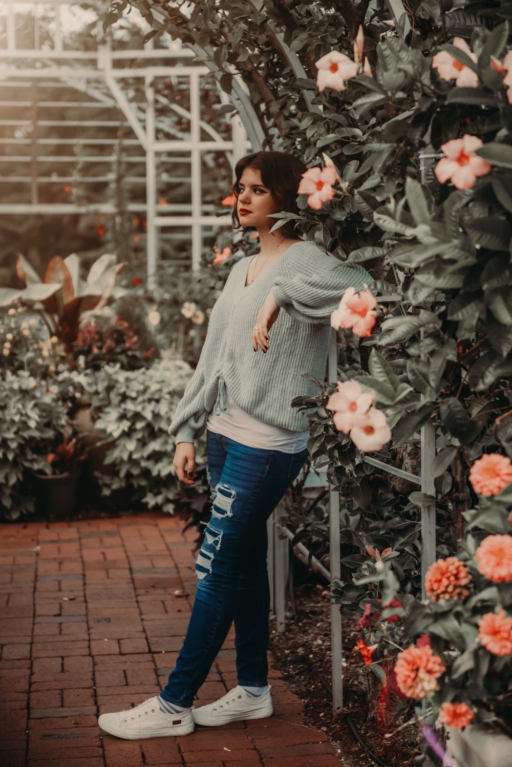 Artistic portrait in garden setting with pink flowers and brick wall backdrop.