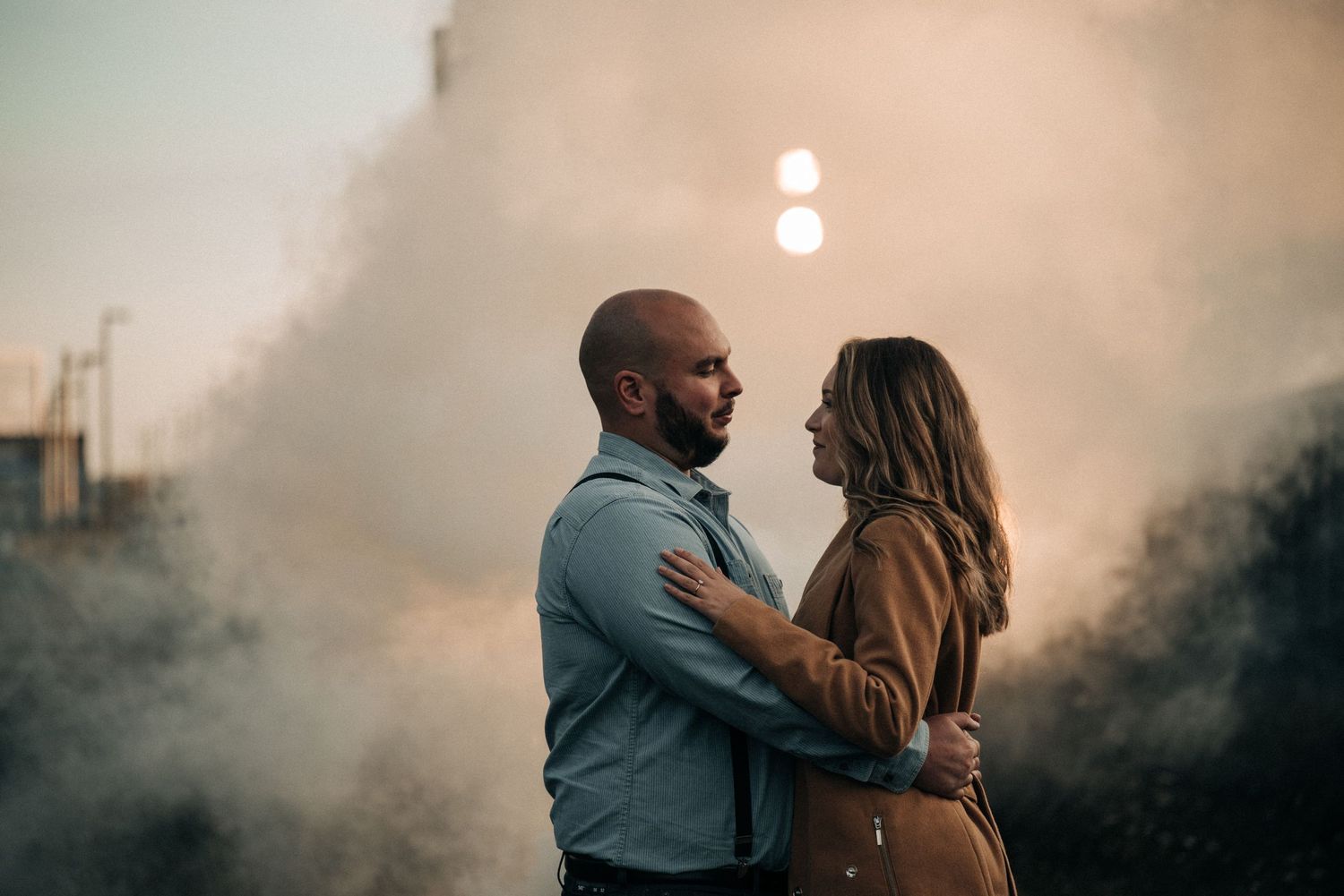 A couple shares a romantic moment surrounded by atmospheric fog at sunset.