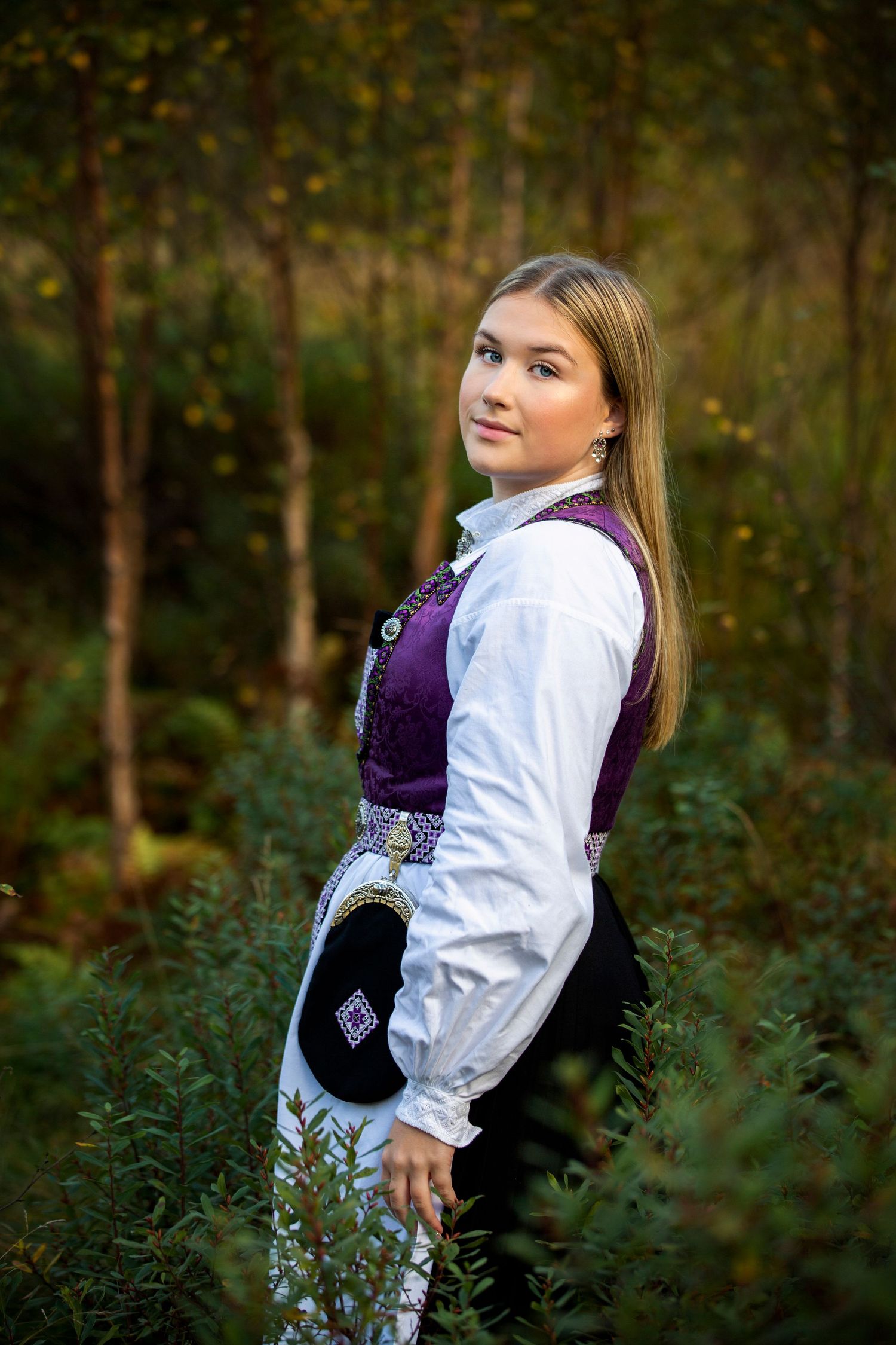Woman in traditional Norwegian folk costume posing in forest setting.