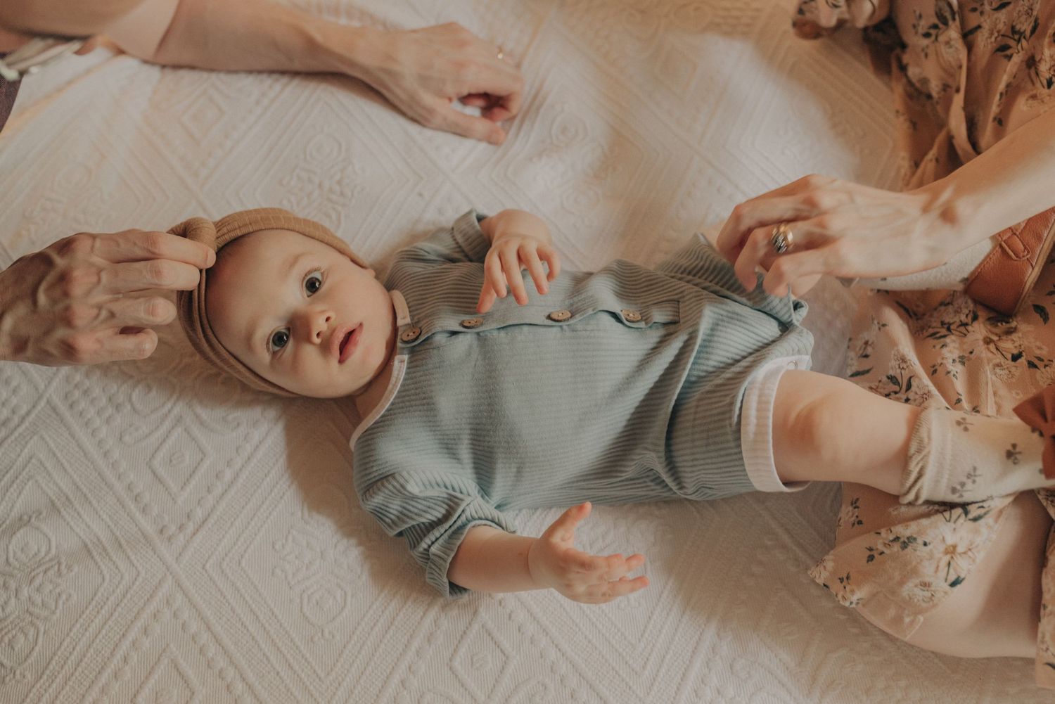 Baby in light blue onesie lying on white blanket.