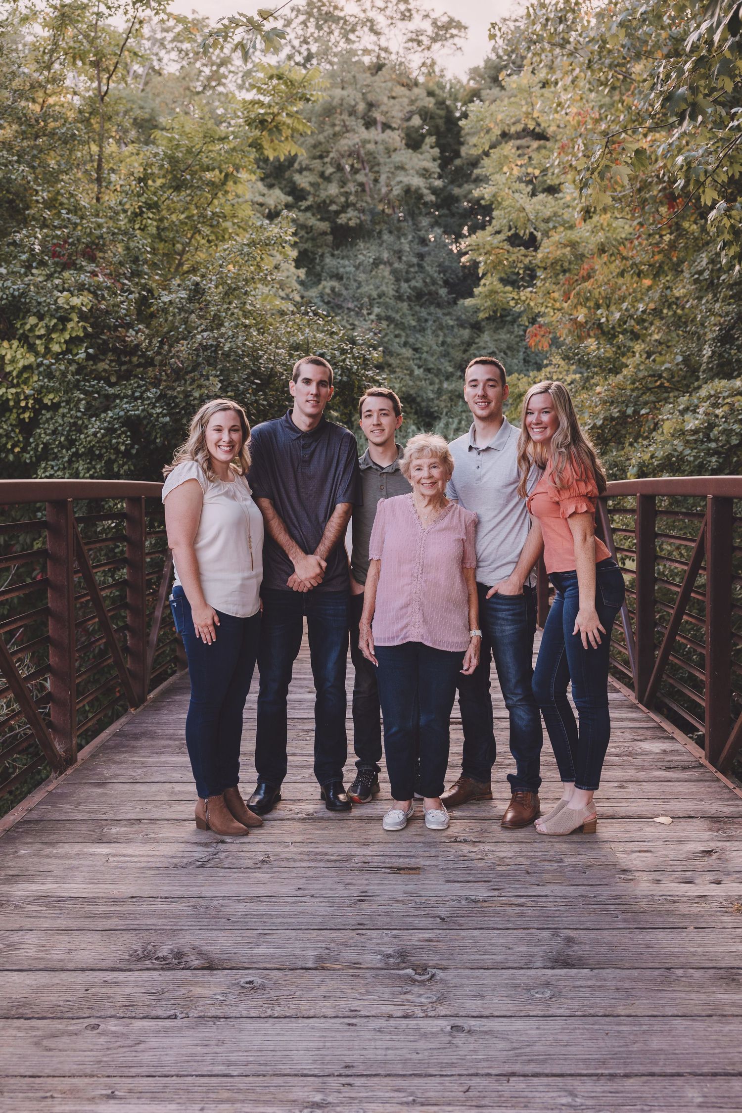 Multi-generational group poses for a family portrait on a wooden bridge surrounded by autumn trees.