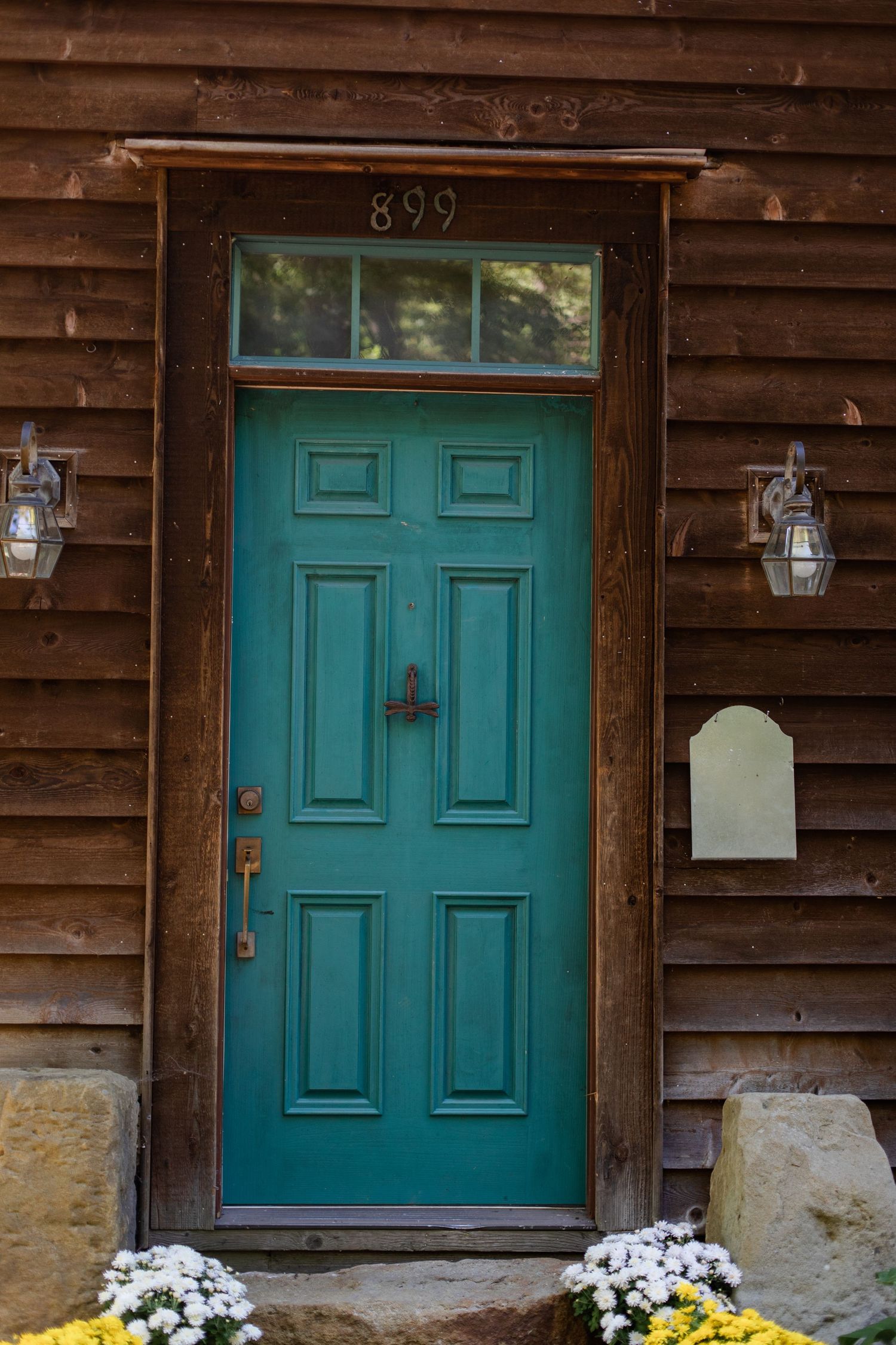 Turquoise door with lanterns on brown wooden cabin exterior and white flowers below.