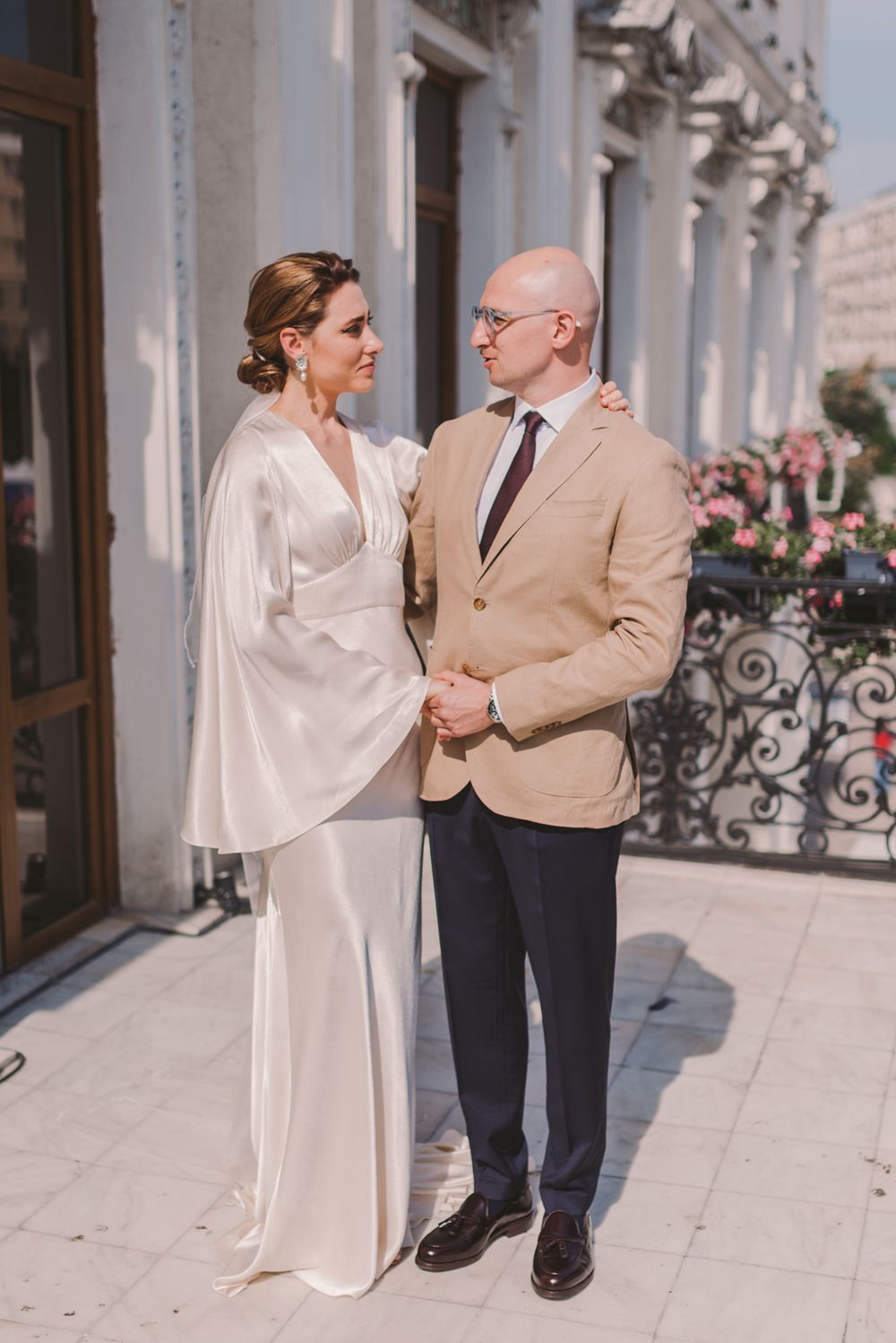 Couple dances on elegant white columned balcony in light colored formal attire.
