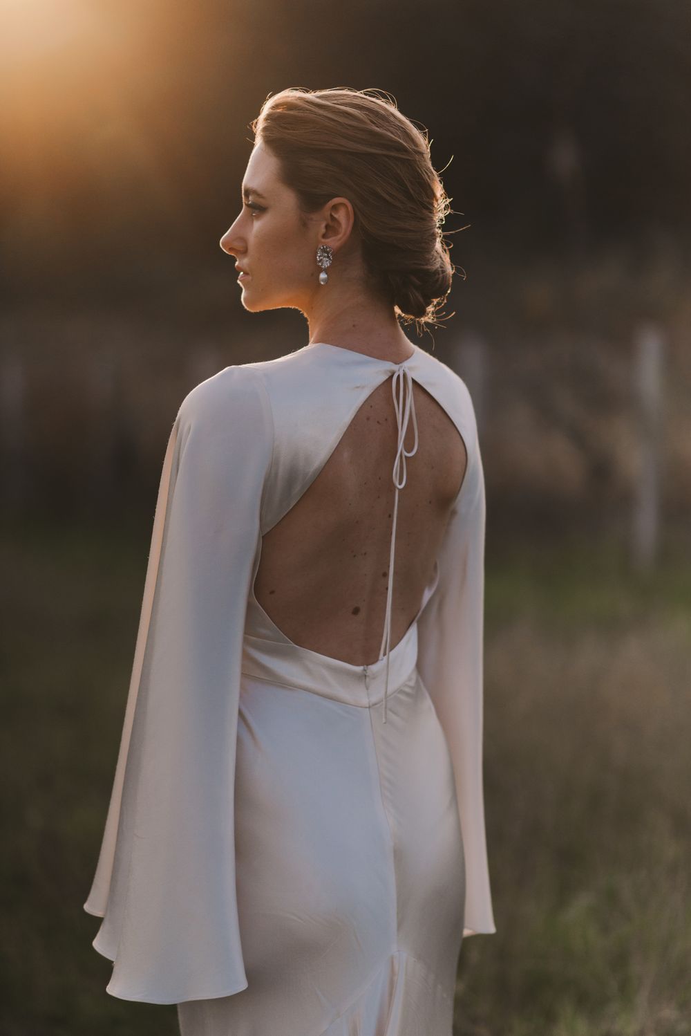 Elegant white wedding dress with bell sleeves and open back design captured at sunset.