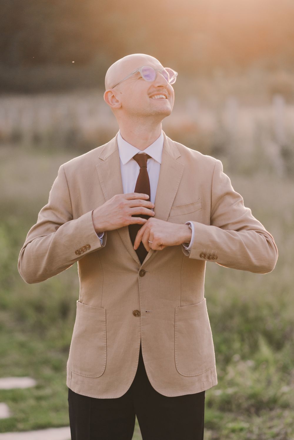 Person in tan suit jacket adjusts their tie in a sequence of casual poses outdoors.