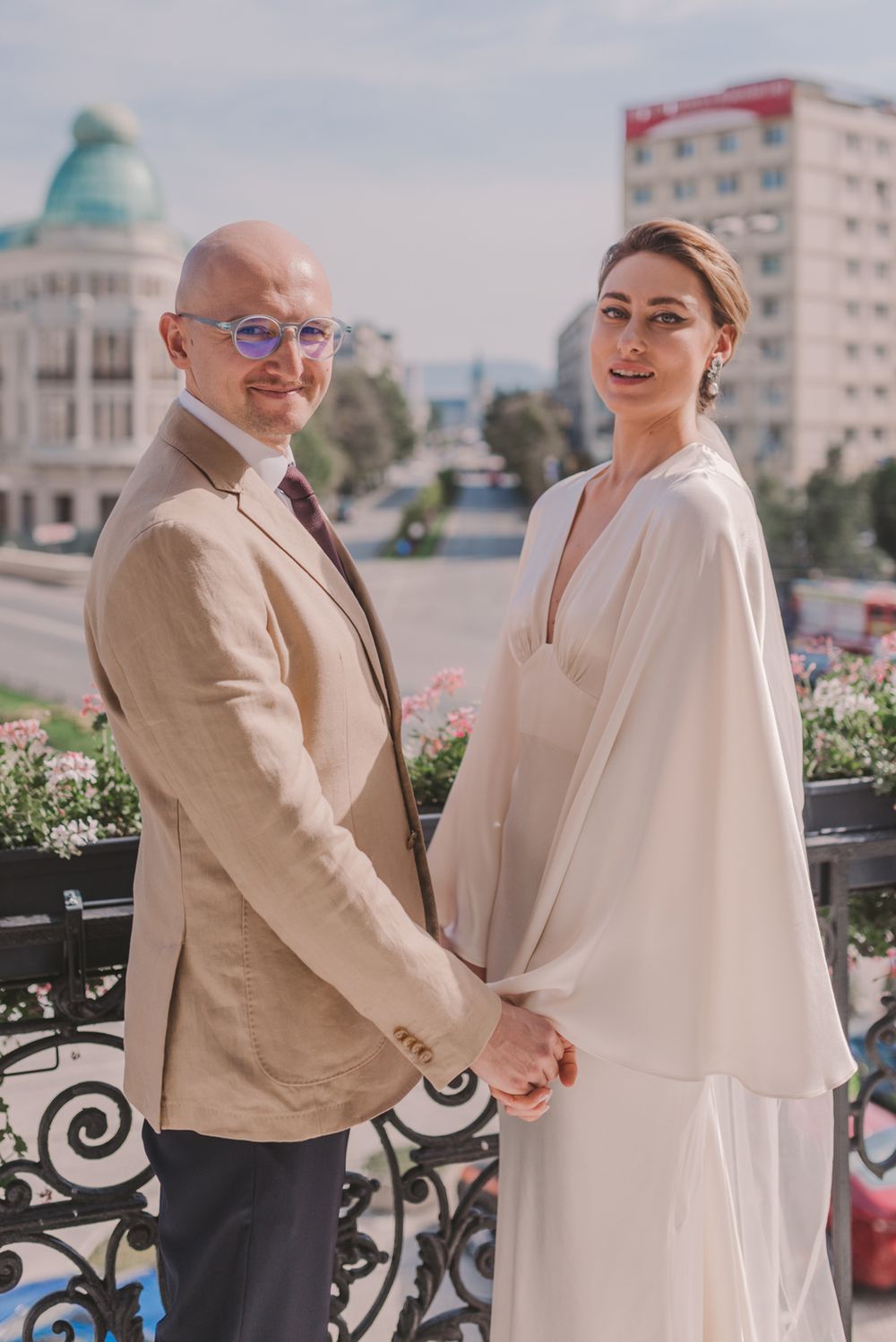 Couple in light-colored formal wear shares romantic moment on urban balcony.