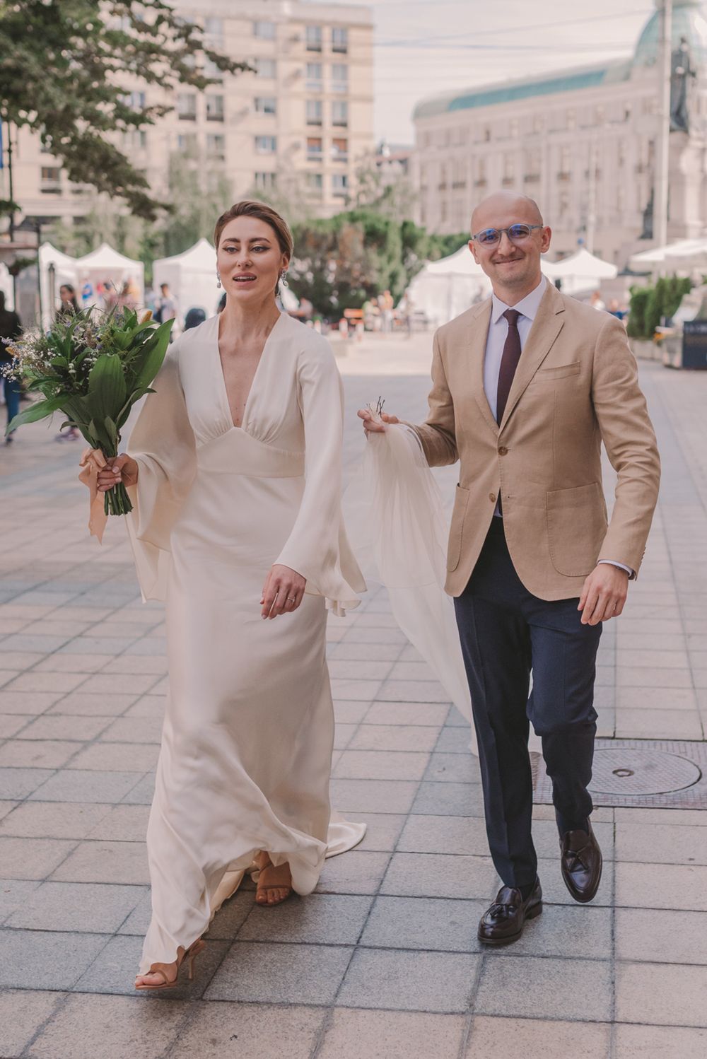 A couple dances playfully on a city sidewalk with urban buildings in the background.