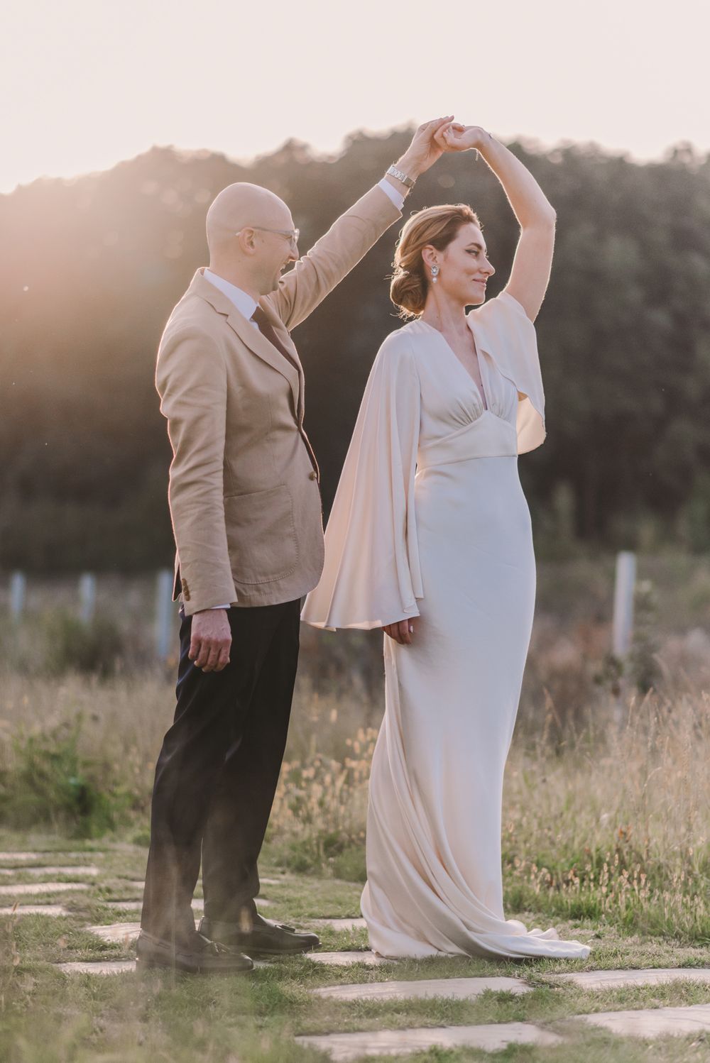 A couple dances together in a sunlit field with tall grass and natural lighting.