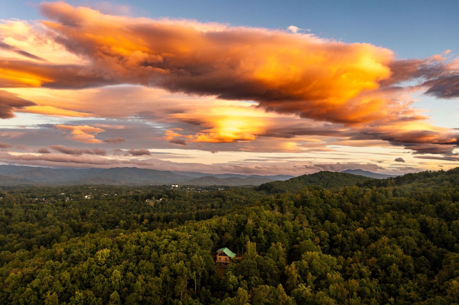 Dramatic sunset panorama with orange and pink clouds stretching across mountain landscape.