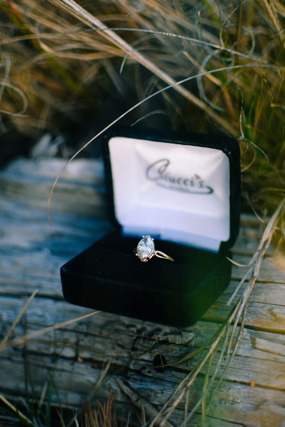 Diamond engagement ring in black velvet box nestled in tall grass.