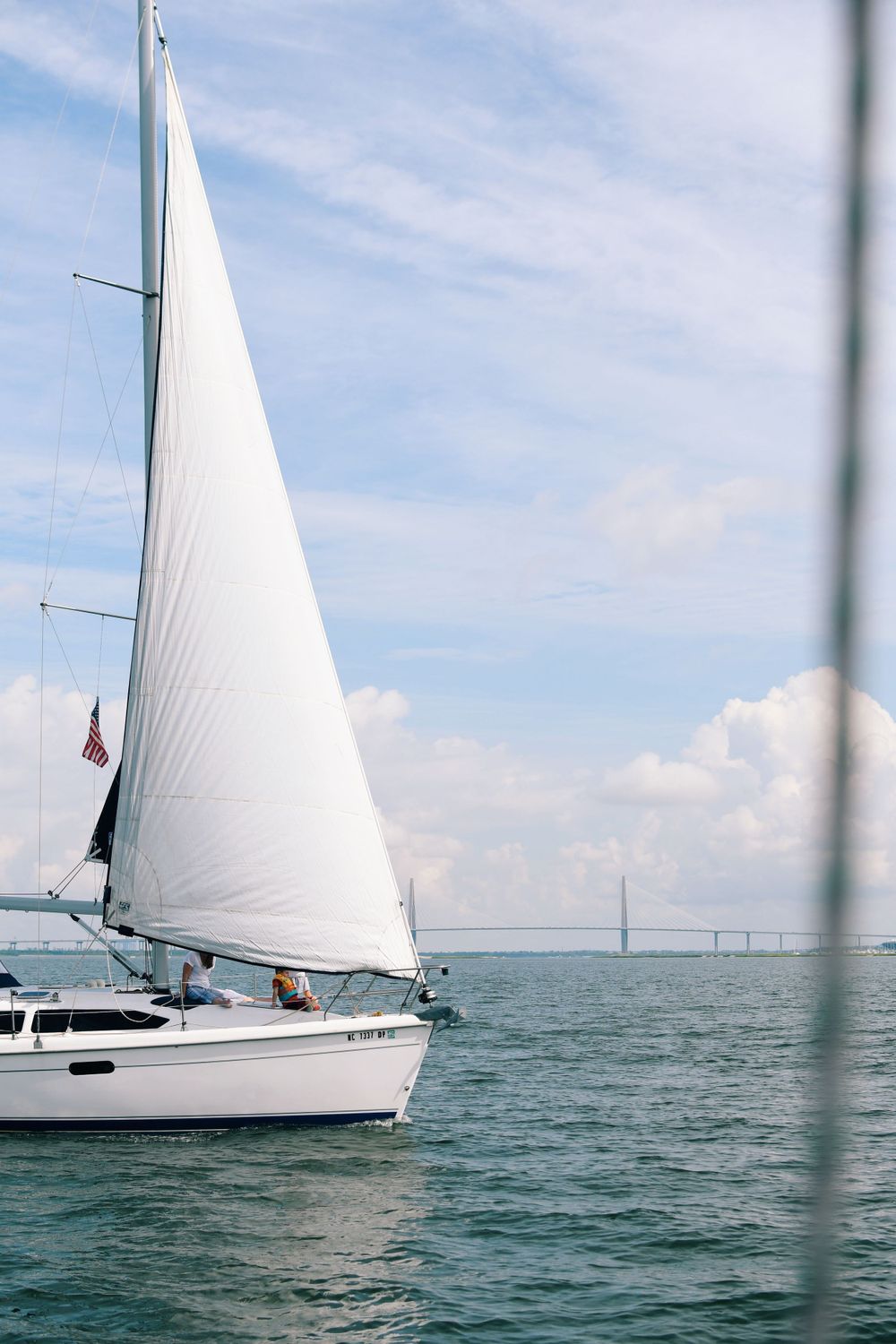 White sailboat cruising on calm waters with bridge visible in distance.