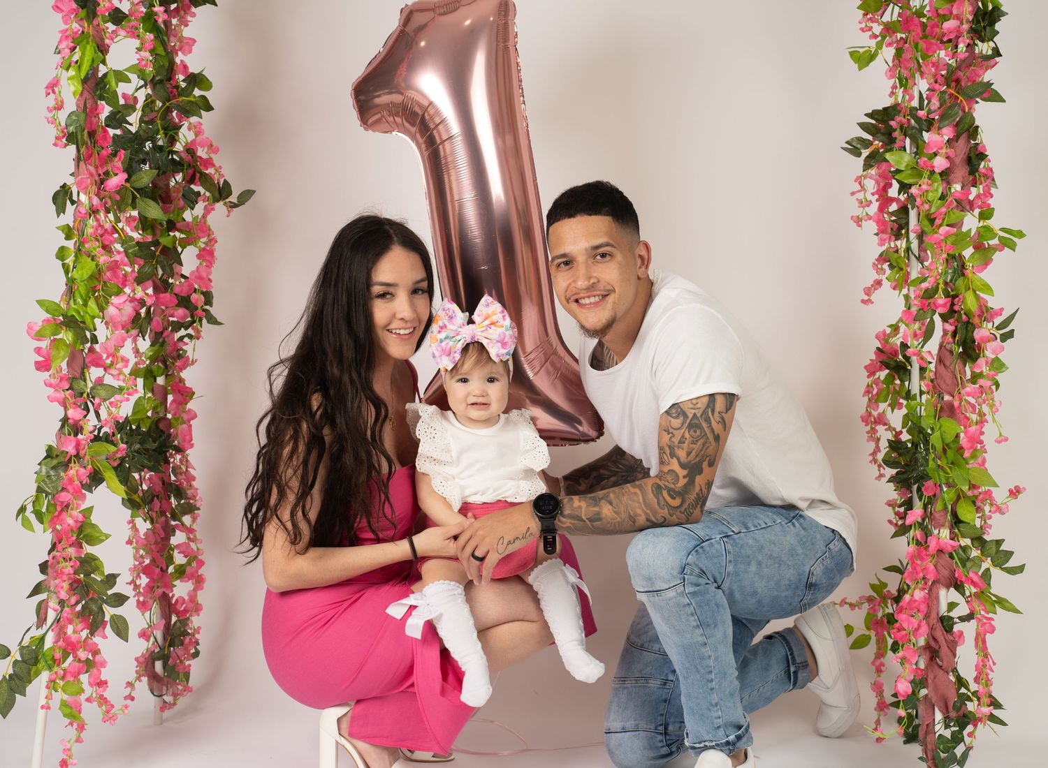 Baby photo session setup with pink floral arch and rose gold number decorations.