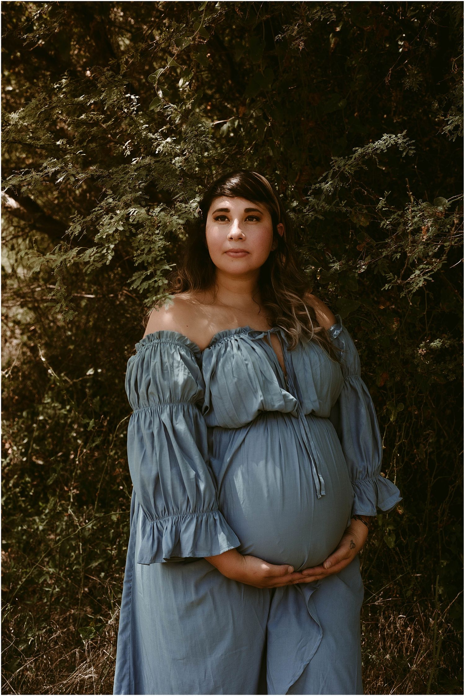 Artistic maternity photo against textured rock wall wearing blue peasant dress.