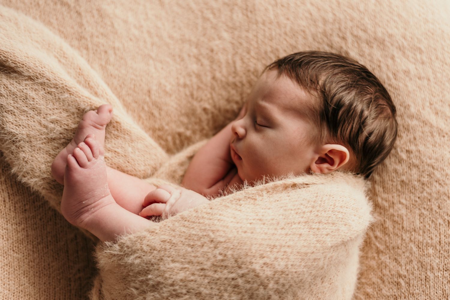 Sleeping baby nestled in soft beige blanket showing peaceful expression.