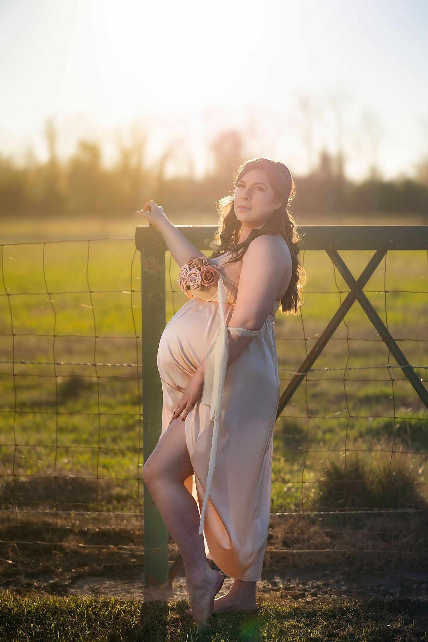 Expectant mother in a flowing maternity gown posing gracefully at sunset in a rural field, exemplifying maternity photog