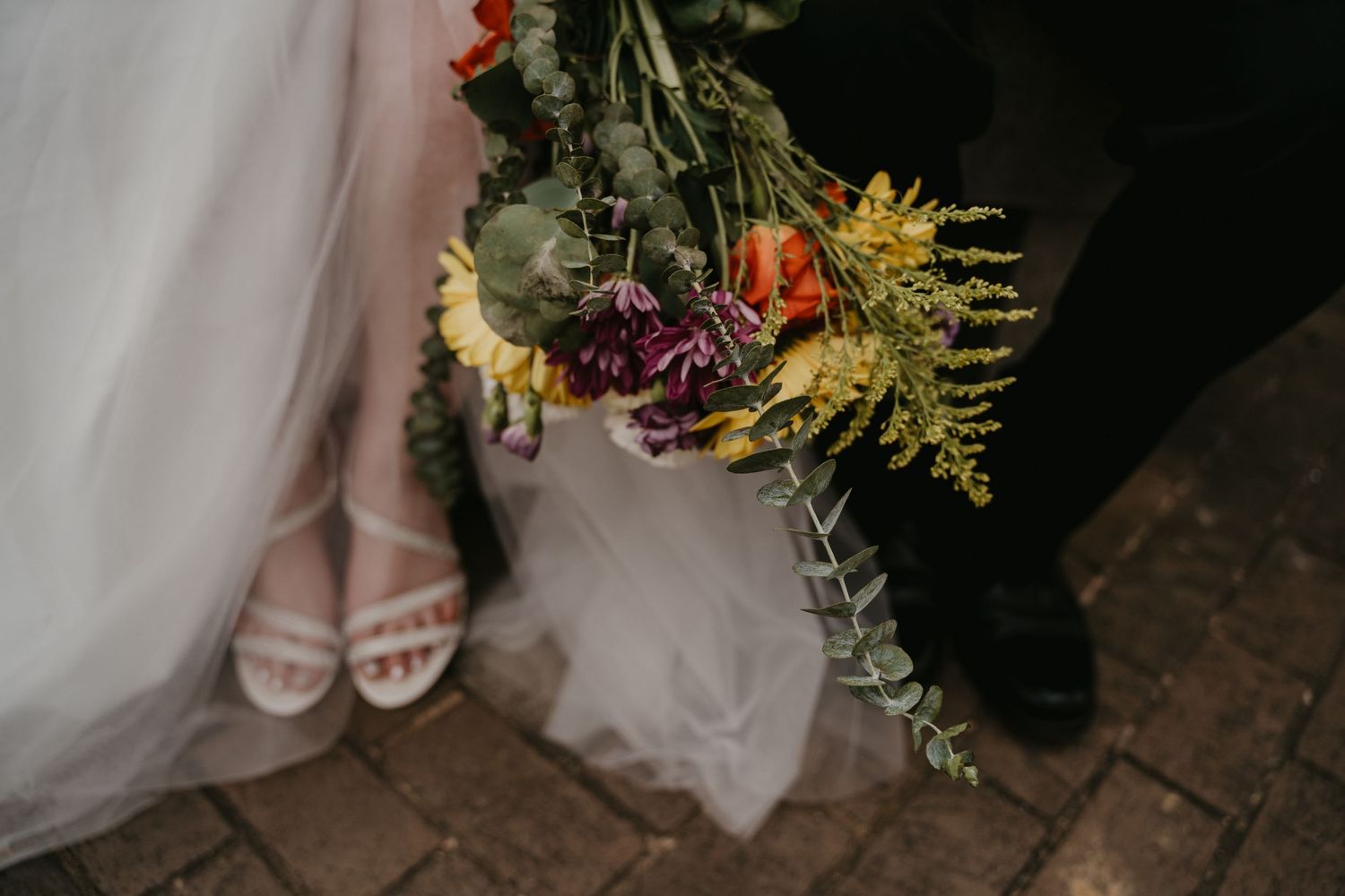 Bride and grooms feet while sitting on a bench holding bouquet