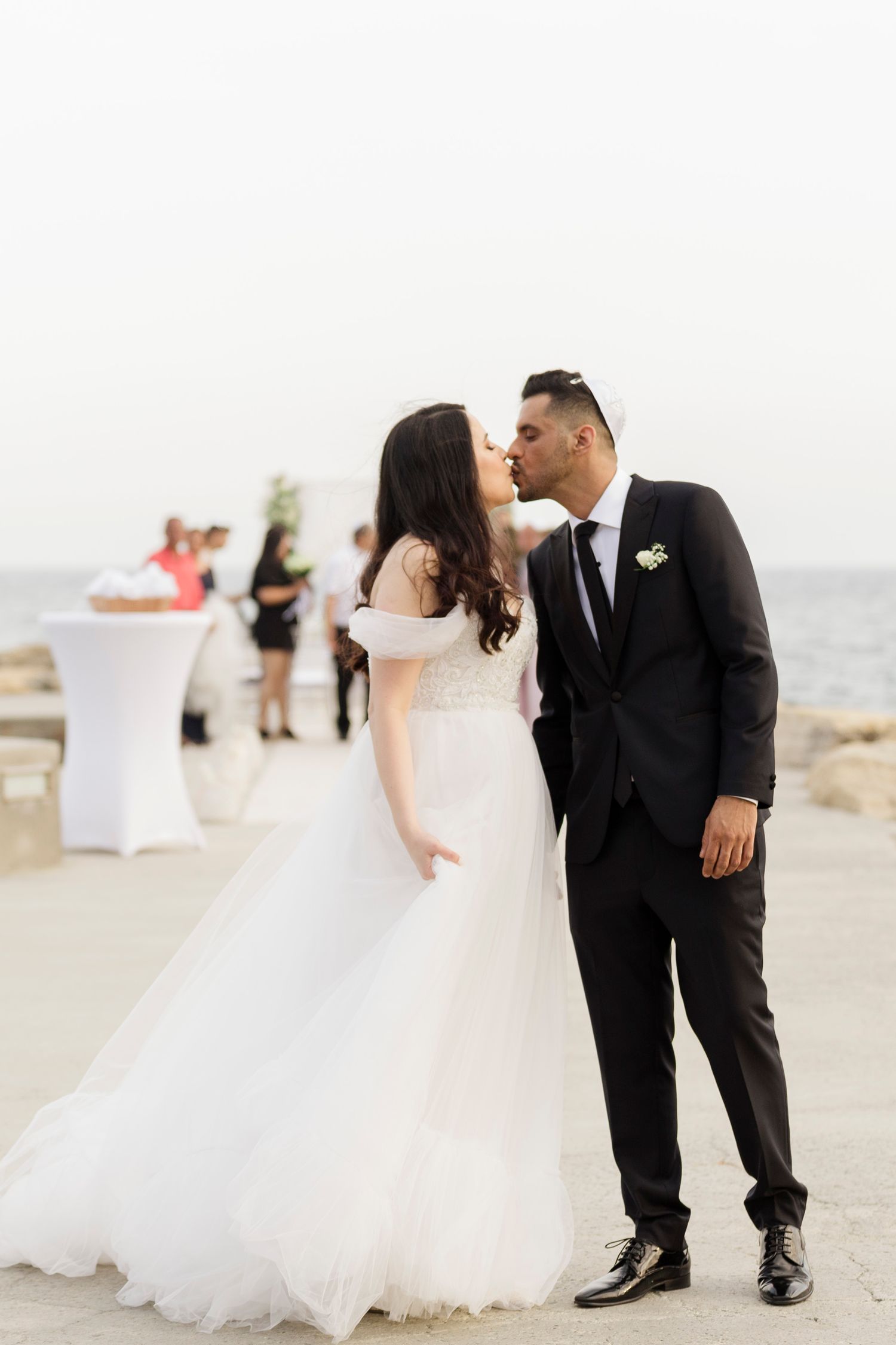 Bride and groom kiss on beach with ocean in background.
