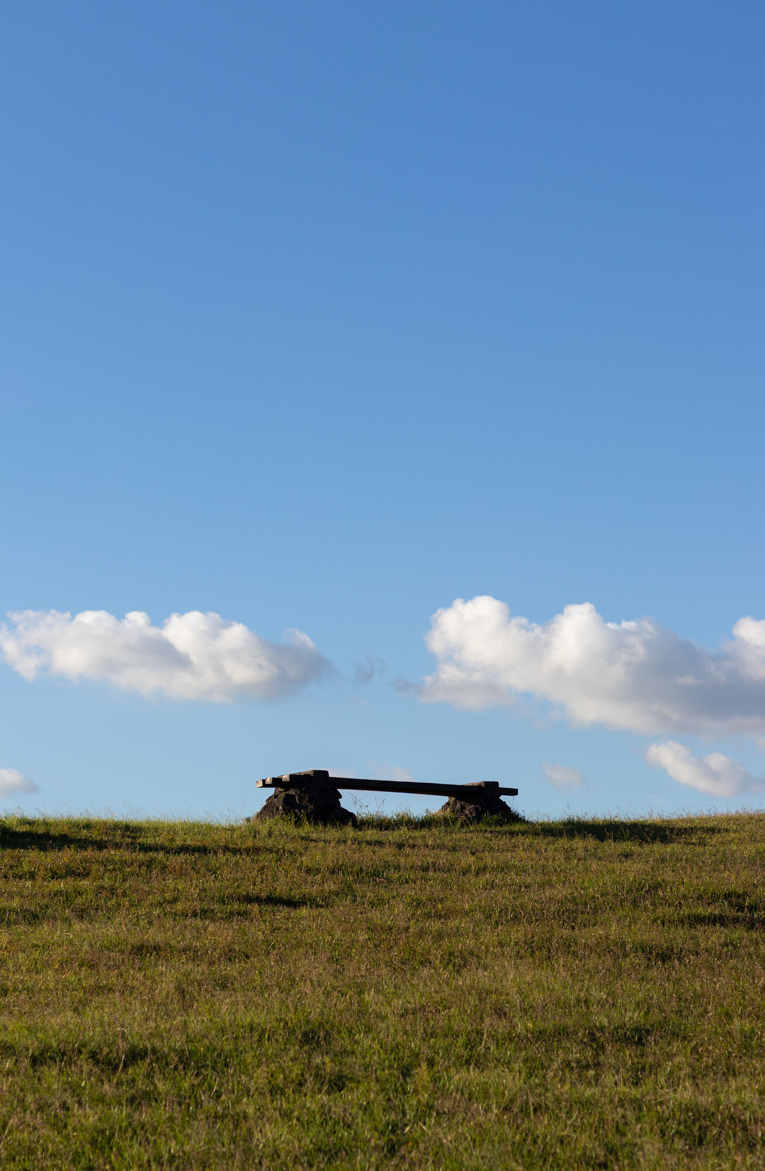 Ancient stone dolmen structures sit atop a grassy hilltop against a bright blue sky with white clouds.