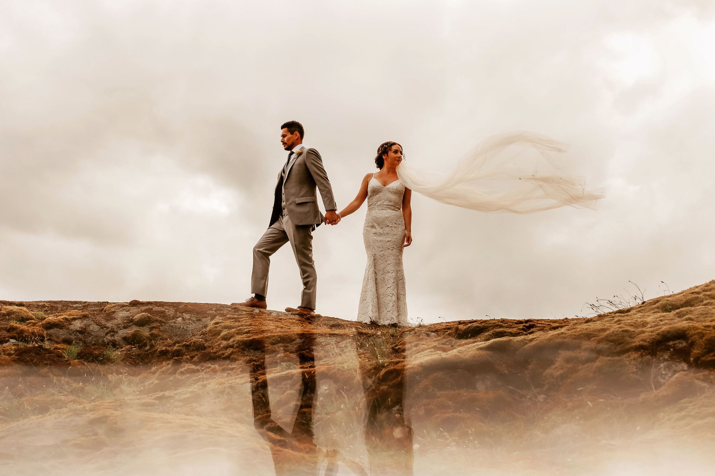 Couple walking hand in hand along a scenic beach at sunset with dramatic clouds in the background.
