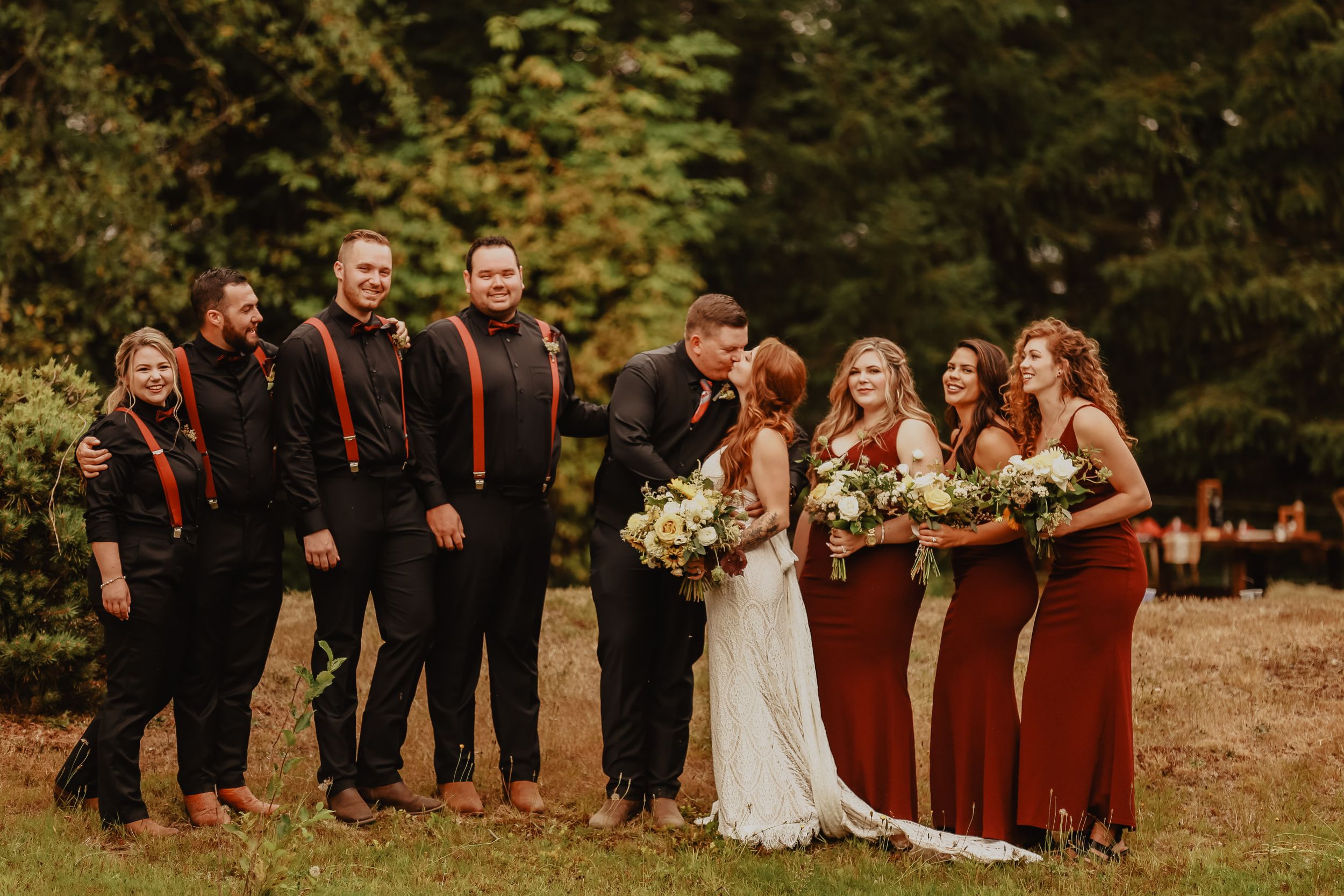 Wedding party in burgundy and black attire posing together against an autumn forest backdrop.