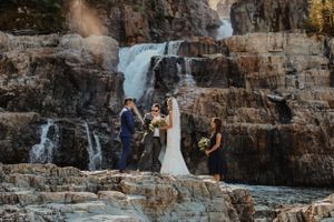 Wedding ceremony taking place in front of majestic waterfall on rocky terrain.