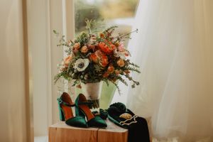 Elegant floral arrangement with emerald shoes displayed on wooden surface.