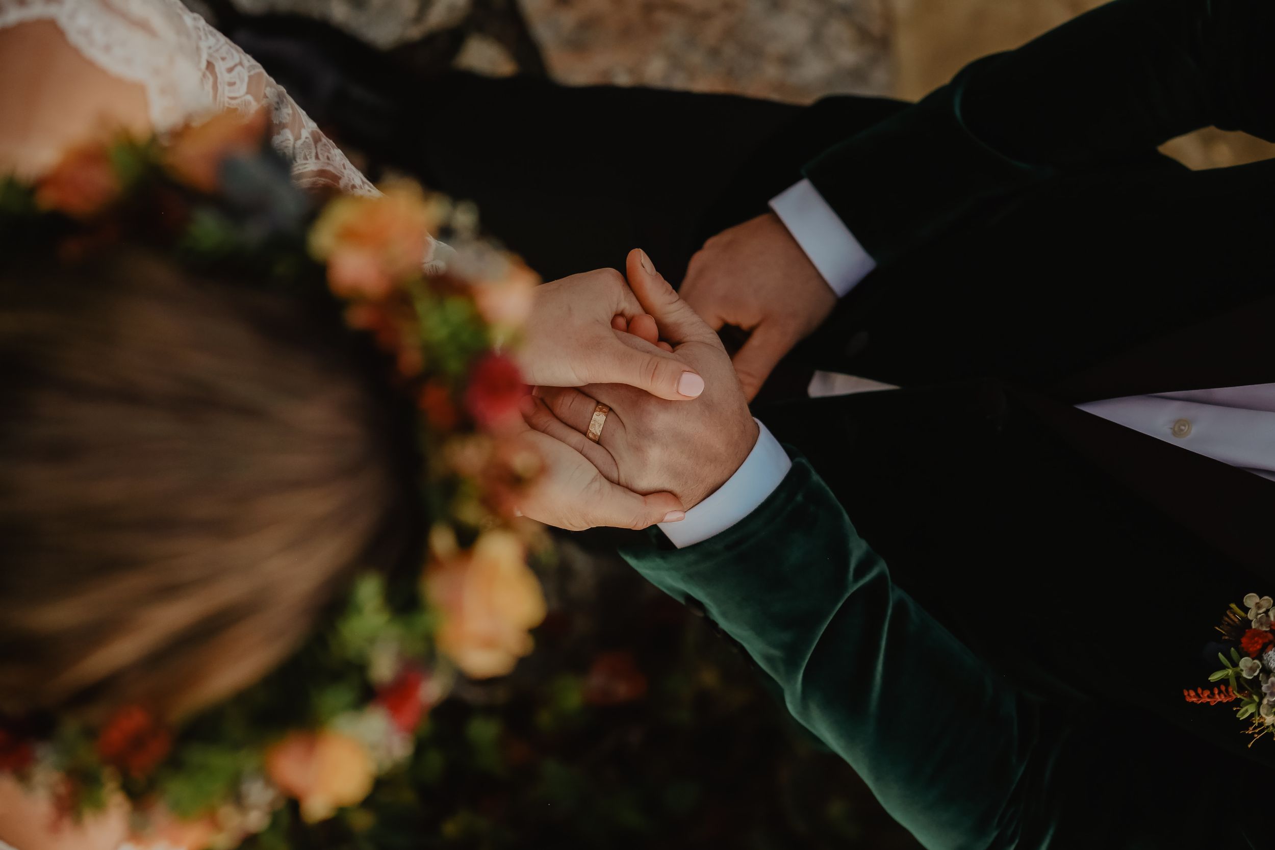 Intimate moment captured with joined hands against floral backdrop.