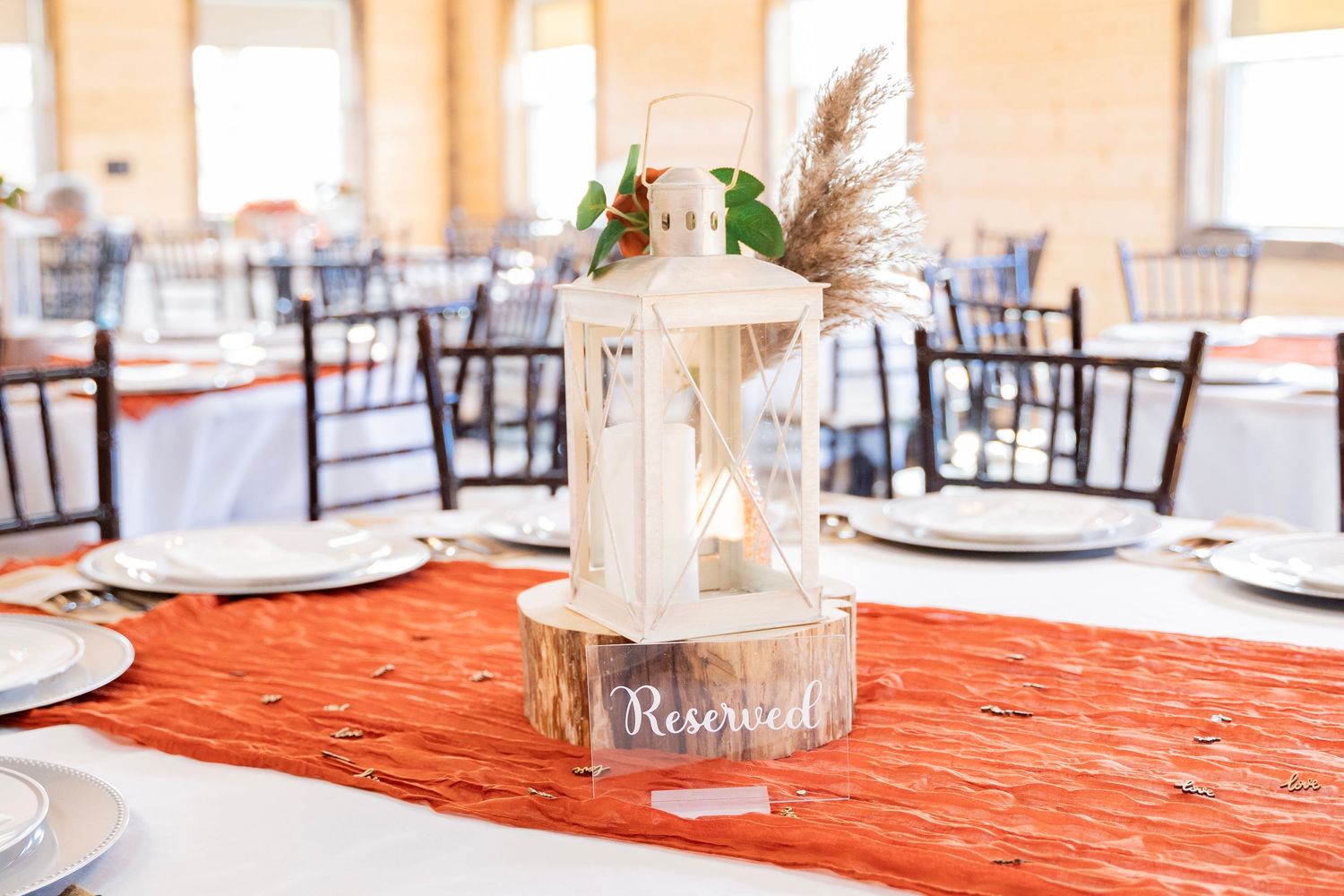 Elegant white lantern centerpiece with pampas grass on a rust-colored table runner at a wedding.