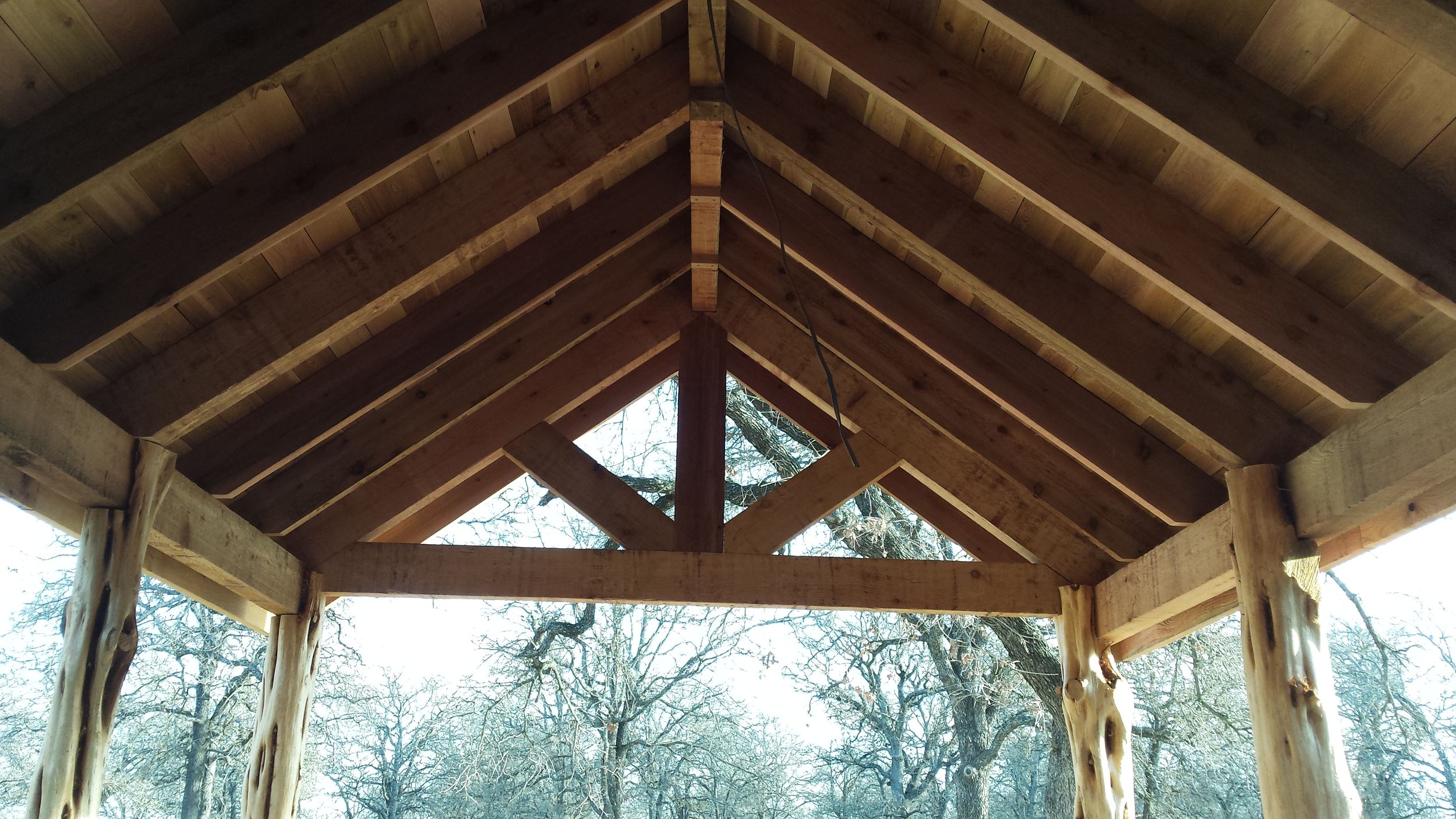 A rustic wooden gazebo with exposed beams and rafters overlooks a scenic mountain landscape in winter.