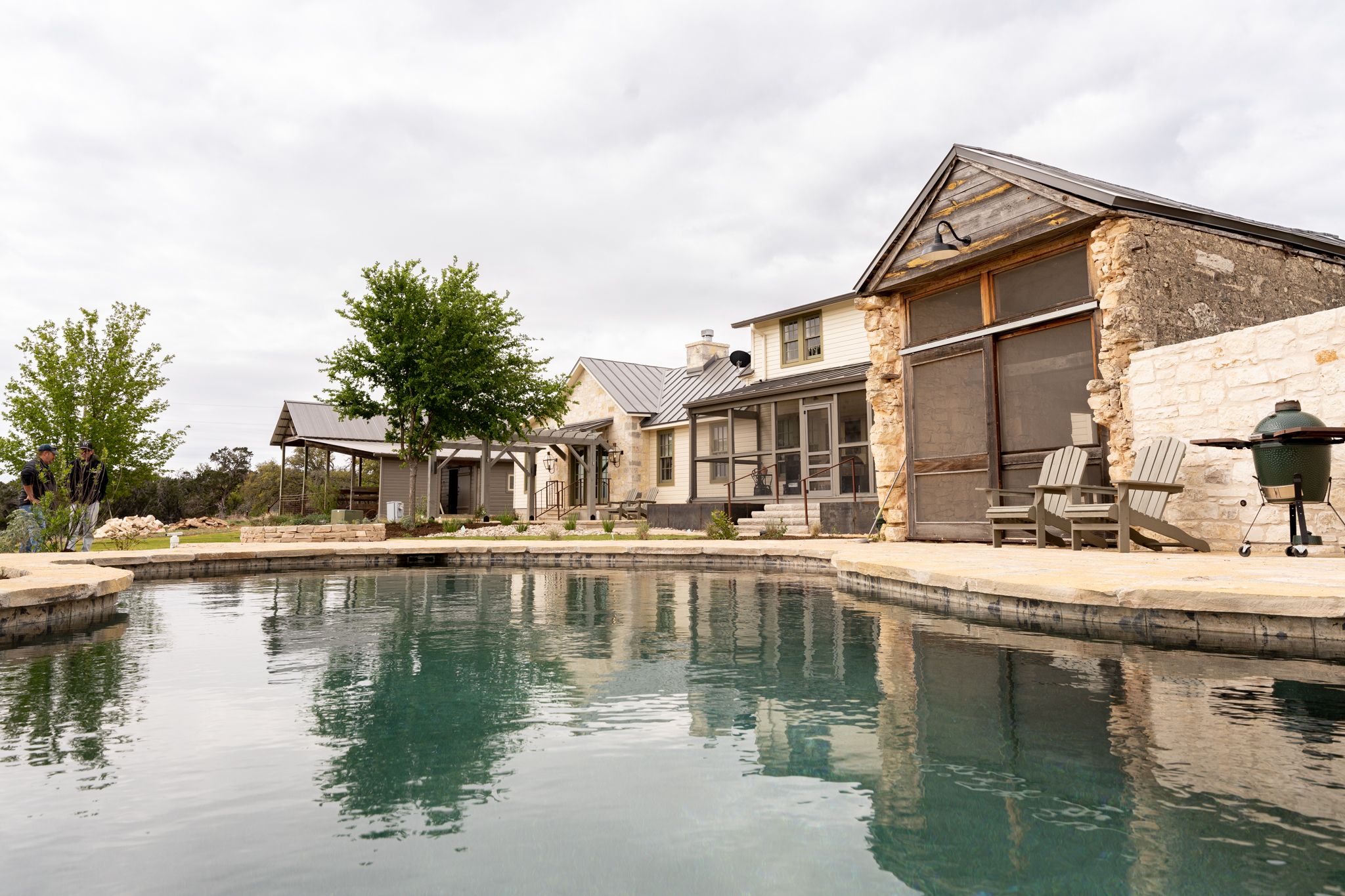 Modern luxury home exterior with stone facade and large swimming pool reflecting the overcast sky.
