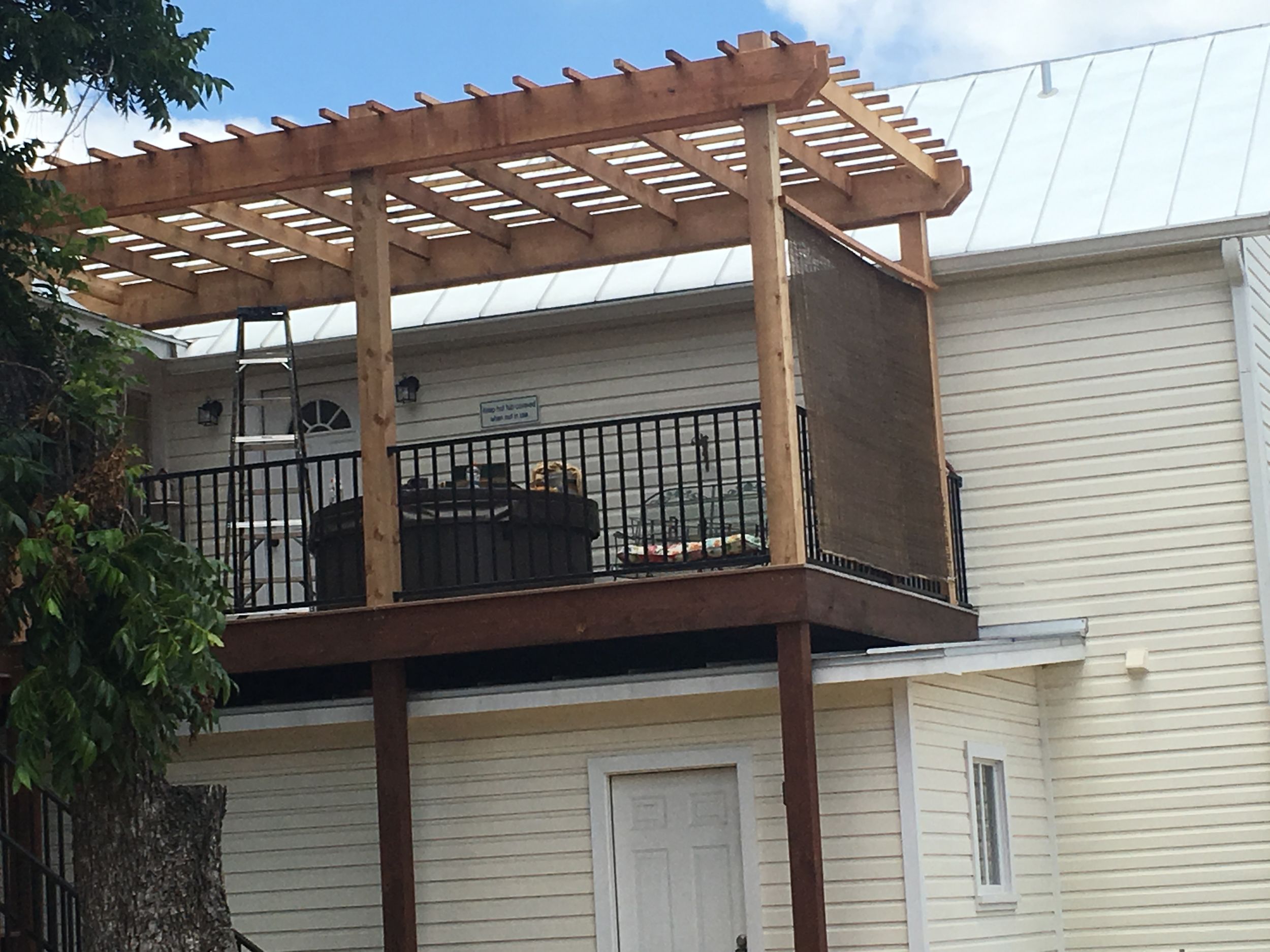 Wooden pergola with lattice roof extends from white house siding, creating a shaded outdoor living space.